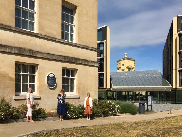 Photo of Thelma Sanders, Xante Cummings and Dr Peggy Frith standing in front of a plaque mounted on the outside of the Radcliffe Humanities Building