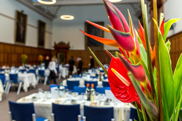 Landscape photo of a large room set up for a formal dinner with bright tropical flower in the foreground