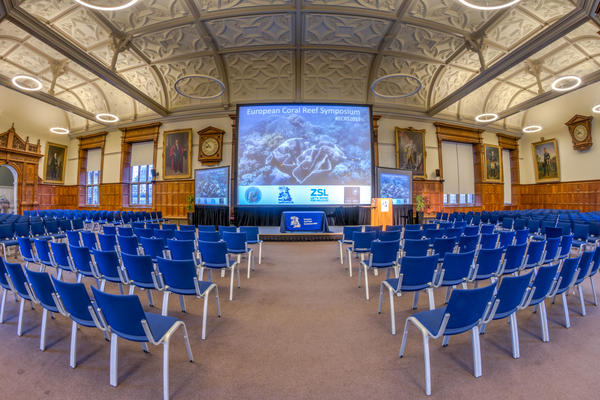 Photo of a room set up for a conference, with rows of chairs and a large screen above the stage