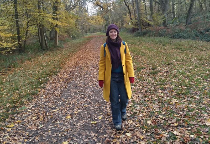Photo of Alice Little standing in a woodland surrounded by autumn leaves