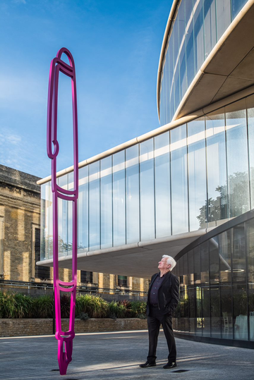 Artist Sir Michael Craig-Martin posing alongside large pink fountain pen sculpture outside Blavatnik School of Government