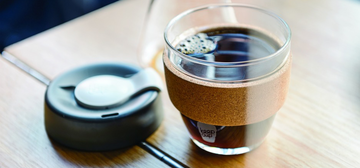 Photo of black coffee in a glass with a cork sleeve and a plastic lid