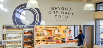 Photo of a cafe with 'Beyond Ordinary Food' text and logo on a white wall above the serving hatch