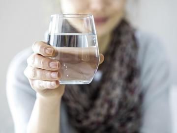Close up photo of a glass of water being held by a woman in the background
