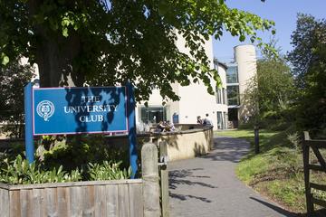 Landscape photo of a blue sign reading 'The University Club' in white text, with the Club building and path leading up to it in the background