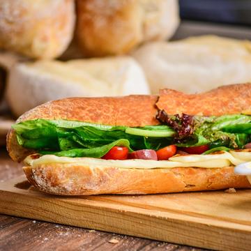 A baguette filled with cheese and salad on a bread board